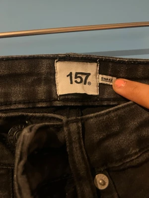Svarta skinny jeans från 157 - Svarta skinny jeans från 157 med klassisk femficksdesign och dragkedjegylf. Jeansen har en tight passform och är tillverkade i ett stretchigt jeanstyg som sitter snyggt på benen. Perfekta för en trendig och stilren look.