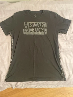 Svart Armani Exchange t-shirt - Cool svart t-shirt från Armani Exchange med stort tryck på bröstet i grått. Klassisk rund halsringning och korta ärmar. Perfekt för dig som gillar stilrena och trendiga plagg med tydlig logga.