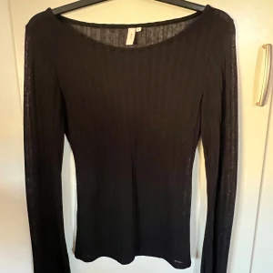 Svart ribbad långärmad topp Nelly - En svart, ribbad långärmad topp från Nelly med rundad halsringning. Tunn och stretchig modell som sitter snyggt och passar perfekt till jeans eller kjol. Enkel och stilren design som är lätt att matcha.