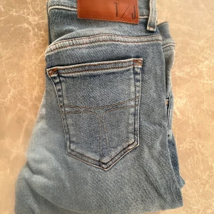Ljusblå  jeans från Tiger of Sweden - Säljer ett par ljusblå  jeans från Tiger of Sweden med klassisk femficksdesign och snygga slitningar. Jeansen har normal midja och är tillverkade i mjukt denimtyg med stretch för extra komfort. Perfekta för dig som gillar en smal passform och stilren look.