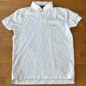 Vit pikétröja från Tommy Hilfiger - Klassisk vit pikétröja från Tommy Hilfiger med liten broderad logga på bröstet. Tröjan har korta ärmar, krage och knappar framtill. Regular fit stretch för extra komfort. Perfekt för en clean och stilren look.