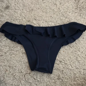 Mörkblå bikini med volangdetaljer - Supersnygg mörkblå bikini med volangdetaljer både på toppen och trosorna. Bikinin har en enkel och stilren design med breda axelband och mjukt material som sitter skönt. Perfekt för strandhäng och poolparty i sommar! 💙(OANVÄND) 