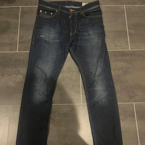 Mörkblå Diesel Buster jeans - Säljer ett par mörkblå Diesel Buster jeans med klassisk femficksdesign och snygga kontrastsömmar. Jeansen har en rak passform och subtila slitningar framtill och baktill för en cool look. Perfekta för dig som gillar stilrena och tidlösa jeans.