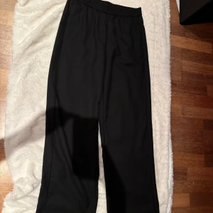 Svarta wide byxor från Gant, strl 38 - Svarta byxor från Gant i storlek 38 med elastisk midja och sidofickor. Modellen är wide och har en avslappnad passform. Materialet känns som en mjuk bomullsblandning, perfekt för en chill och stilren look.