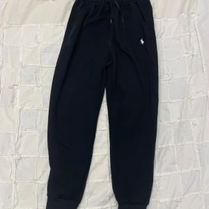 Svarta mjukisbyxor Polo Ralph Lauren XL - Svarta mjukisbyxor från Polo Ralph Lauren i storlek XL. Slim fit med resår och snörning i midjan, ribbade muddar vid benslut och klassisk vit logobrodyr på vänster höft. Sköna och stilrena, perfekta för chill eller träning.