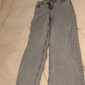 Gråa wide jeans från Hailys - Säljer ett par ljusgrå jeans från Hailys i storlek 40. Jeansen har raka, vida ben och klassisk femficksdesign. Tillverkade i denim med bälteshällor och knappstängning framtill. Perfekta för en avslappnad och trendig look. Dem är ett mellanting mellan högmidjade och lågmidjade. Knappt använda. W30