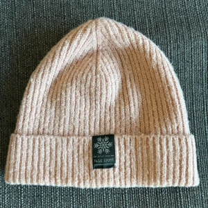 Ljusrosa ribbad mössa från Falk Sport (Glitter) - Mysig ljusrosa ribbstickad mössa från Falk Sport (Glitter) med uppvikt kant och snygg snöflinge-logga framtill. Tillverkad i mjuk syntetblandning med lite stretch för skön passform. Använd men i bra skick och tvättad flera gånger.