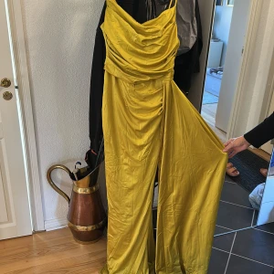 Gul långklänning i satin - Maxiklänning. Snygg gul långklänning i glansigt satinmaterial med draperad överdel och smala axelband.