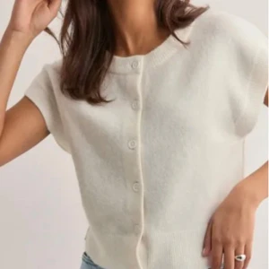 Vit kortärmad kofta med knappar - Superfin vit kofta med korta ärmar och rund hals. Tröjan har knappar hela vägen framtill och är stickad i ett mjukt material. Perfekt att slänga över ett linne eller t-shirt för en chill och clean look.