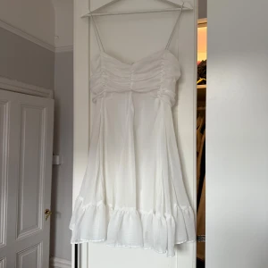 Vit volangklänning  - Superfin vit kortklänning från Chiquelle med tunna axelband, rynkad överdel och volangkant nertill. Klänningen passar dig som kan ha M/L. Klänningen skulle används till min student men det blev tyvärr inte så. Den har däremot används vid 2 andra tillfällen!🩷