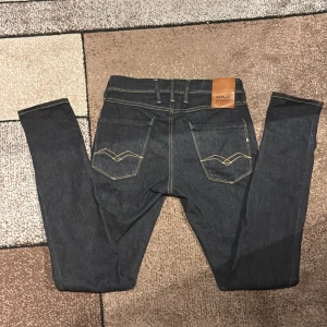 Replay Hyperflex Anbass jeans, mörkblå - Snygga Replay Hyperflex Anbass jeans i mörkblå tvätt med kontrastsydda bakfickor och läderpatch i midjan. Slim fit-modell med medelhög midja och stretchigt material för extra komfort. Perfekt för dig som gillar stilrena och moderna jeans.