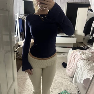 Mörkblå långärmad topp med utsvängda ärmar - Säljer en mörkblå långärmad topp med utsvängda ärmar och figurnära passform. Toppen har en enkel, stilren design med rund hals och är gjord i ett mjukt, stretchigt material som sitter snyggt mot kroppen. Perfekt för dig som gillar minimalistisk stil.