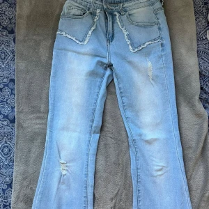 Ljusblå bootcut jeans med slitningar - Snygga ljusblå jeans med bootcut passform och slitna detaljer på fickor och ben. Jeansen har fransade kanter vid fickorna och lätt tvättad look. Perfekta för en avslappnad och trendig stil.