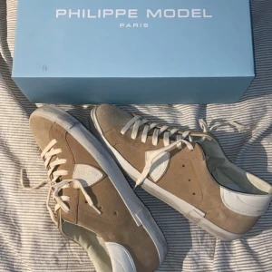 Philippe Model beige sneakers - Snygga sneakers från Philippe Model Paris i beige mocka med vita skinnpaneler och vit platt sula. Klassisk låg modell med rund tå och snörning. Märkeslogga på sidan och hälen. Perfekta för dig som gillar stilrena och exklusiva sneakers. Nypris 3799kr. Pris kan diskuteras. Original förpackning finns. Skriv om du har några funderingar.