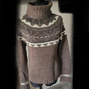 Brun stickad polotröja med mönster - Säljer en brun stickad polotröja med höga ribbade krage och snyggt mönster i vitt och grått över axlar och ärmar. Tröjan har lång ärm och är perfekt för kalla dagar. Klassisk nordisk stil som är både mysig och trendig.