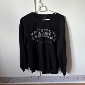 Svart sweatshirt med Los Angeles-tryck - Svart sweatshirt med vit text 'Los Angeles California' på bröstet. Klassisk rund halsringning och långa ärmar. Perfekt för en avslappnad streetstyle-look. Mjuk och skön, troligtvis i bomullsmix.