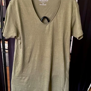 Olivgrön v-ringad t-shirt Primark XS - Olivgrön t-shirt från Primark i slim fit-modell. T-shirten har v-ringning, korta ärmar och är tillverkad i 100% bomull. Enkel och stilren design som passar perfekt till jeans eller shorts.