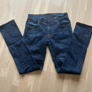 Mörkblå Nudie Jeans, W31 L34 - Snygga mörkblå jeans från Nudie Jeans med klassisk femficksdesign och kontrastsömmar. Modellen har raka ben och subtila broderade detaljer på bakfickorna. Passar dig som gillar stilrena och tidlösa jeans med bra passform.