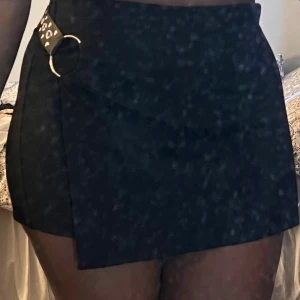 Svarta omlottshorts med ringdetalj från New Yorker - Snygga svarta shorts från NA-KD med omlott-design framtill och cool ringdetalj i midjan med nitar. Högmidjade och tight passform som framhäver figuren. Perfekta för dig som gillar en edgy och trendig stil.
