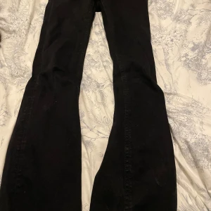 Svarta bootcut jeans från Gina Tricot - Svarta jeans från Gina Tricot i storlek 170. Modellen har bootcut-ben som ger en snygg siluett och är tillverkade i ett klassiskt jeanstyg. Perfekt för dig som gillar en lite vidare passform nedtill och vill ha en stilren look.
