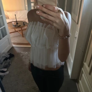 Vit tubtopp med volanger från Vero Moda - Säljer en superfin vit tubtopp från Vero Moda i storlek S. Toppen är axelbandslös och har flera lager med transparent mesh som ger en fluffig och volangig look. Perfekt för dig som gillar romantisk och trendig stil. Elastisk upptill och nertill för skön passform. Använd ca 3 gånger pris kan diskuteras🥰