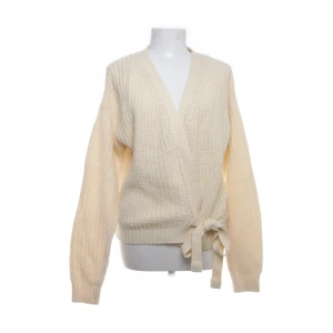 Beige omlott kofta från Ladies Fashion - Säljer en beige stickad kofta från Ladies Fashion i storlek L. Koftan har omlottmodell med knytband i midjan och grovstickad struktur. 