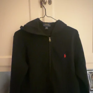  Hoodie från Polo Ralph Lauren - Svart zip up hoodie från Polo Ralph Lauren. storleken är 14-16 vilket motsvarar ungefär 160-170cm lång men lite beroende av vikten också. tröjan är i fint skick men innuti tröjan finns det lite ludd och damm. Tröjan köptes på NK för 1100.