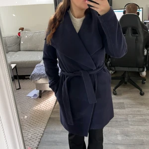 Mörkblå omlottkappa med stor krage - Snygg mörkblå kappa från H&M med stor, svepande krage och omlott-design. Jackan har ett elegant fall och är fodrad på insidan. 