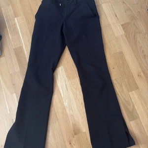 Svarta bootcut-kostymbyxor från BikBok - Snygga svarta bootcut-byxor från BikBok i storlek 34. Byxorna har slits vid benslut och klassisk midja med hällor för bälte. Materialet är mjukt och har en lätt stretch för extra komfort. Perfekt för dig som gillar stilrena och trendiga siluetter.