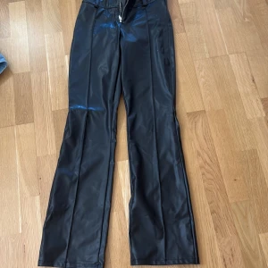 Svarta bootcut skinn utsvängda byxorfrån Gina Tricot - Snygga svarta skinnbyxor  från Gina Tricot i storlek 158. Byxorna har bootcut-snitt och är gjorda i ett skinnliknande syntetmaterial med dragkedja framtill. Perfekta för dig som vill ha en cool och trendig look.