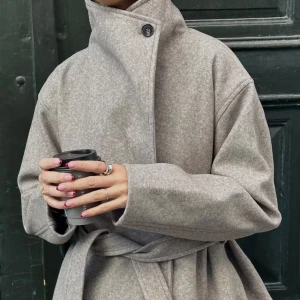 Beige omlott kappa med bälte Gina Tricot - Snygg beige kappa i omlottmodell med bred krage och knytbälte i midjan. Jackan har lång ärm, en knapp vid halsen och är tillverkad i ett mjukt ullblandat tyg. Perfekt för dig som gillar en clean och stilren look. Passar perfekt för höst och vinter och är i storlek L men passar M/XL