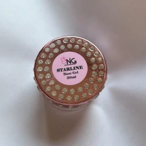 NG Starline Base Gel 30ml med strass - Säljer en NG Starline Base Gel i en burk på 30ml. Burken är rosa med glittriga strasstenar runt om och på locket, vilket ger en lyxig och glam känsla. Perfekt för dig som vill ha snyggt sminkbord och älskar rosa detaljer. Helt ny man ser dock att den är öppnad och lite gele runt om för den har legat med andra geler. 