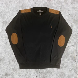 Marinblå tröja med mockadetaljer Polo Ralph Lauren - Marinblå långärmad tröja från Polo Ralph Lauren med bruna mockadetaljer på axlar och armbågar. Klassisk rund halsringning och broderad logga på bröstet. Kom gärna med bud och frågor!