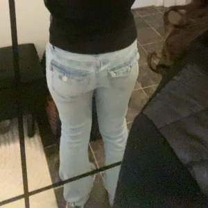 Ljusblå bootcut jeans med låg midja - Säljer ett par ljusblå jeans med bootcut-modell och låg midja. Jeansen har klassiska fickor bak med lock och knappdetaljer. De är jätte low waist och sitter jätte snyggt på mig som har storlek S i byxor. Säljer då jag har för många jeans
