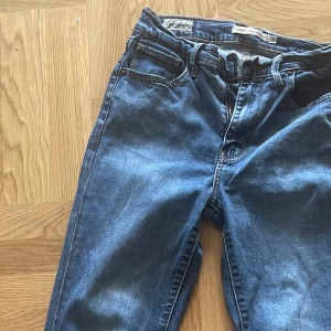 Levi's 504 blå jeans med klassisk passform - Säljer ett par blå Levi's 504 jeans med klassisk rak passform. Strl. Waist 26 -Lenhard 32 , Jeansen har fem fickor, dragkedja och knappstängning med Levi's-logga. Snygga kontrastsömmar och den ikoniska röda Levi's-taggen bak. Perfekta för dig som gillar tidlös denimstil.