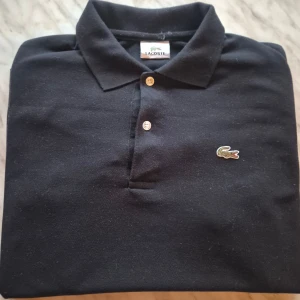 Svart pikétröja Lacoste - Svart pikétröja från Lacoste med klassisk krage och två vita knappar framtill. Skick : 9/10 