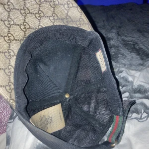 Gucci keps med tigertryck och GG-mönster - Snygg keps från Gucci med klassiskt GG-mönster i beige och brunt, prydd med två coola tigerhuvuden framtill. Justerbar rem med grönt och rött band bak. Materialet är bomull och polyester, perfekt för dig som vill sticka ut med lyxig streetstyle.