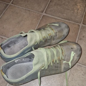 Puma fotbollsskor i ljusgrönt - Säljer ett par lätta fotbollsskor från Puma i ljusgrönt med vita detaljer och snörning. Skorna har mönstrad ovandel och rund tå, samt fasta dobbar för bra grepp på planen. Perfekta för dig som vill sticka ut på matchen!