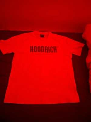 Vit HOODRICH t-shirt med tryck - Säljer en clean vit t-shirt från HOODRICH i storlek L. T-shirten har ett stort svart tryck med HOODRICH på bröstet och klassisk rund hals. Materialet är mjuk bomull och passformen är normal. Perfekt för dig som gillar streetwear och vill ha en enkel men snygg tee.