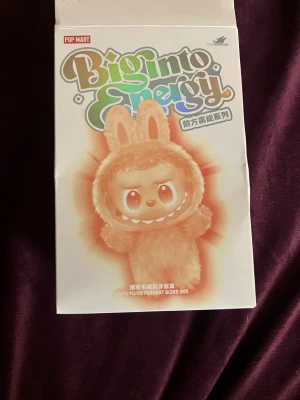 Lila labubu  - Söt och fluffig lila labubu. Labubun har en mjuk och lurvig yta i syntetpäls och är designad för att ge en lekfull och trendig look. Perfekt för dig som vill sticka ut med en unik accessoar.