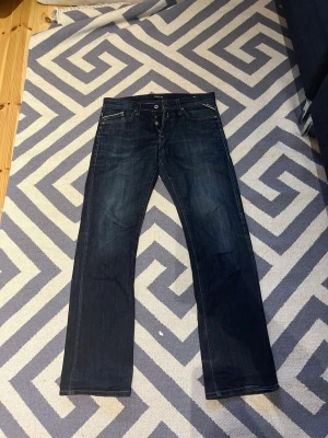 Replay mörkblå jeans straight fit W31 L32 - Säljer ett par mörkblå jeans från Replay i klassisk straight fit. Jeansen har fem fickor, snygga kontrastsömmar och en läderpatch bak i midjan. Materialet är slitstarkt jeans och passformen är normal med raka ben. Perfekta till en avslappnad stil.