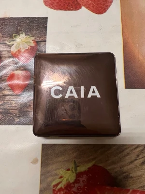CAIA Glow Bronzer Antigua - Säljer en CAIA Glow Bronzer i färgen Antigua. Kommer i en brun, fyrkantig dosa med spegel och har en skimrande varm brun nyans. Perfekt för att ge ansiktet en solkysst look. Innehåller 10 g och är vegansk.