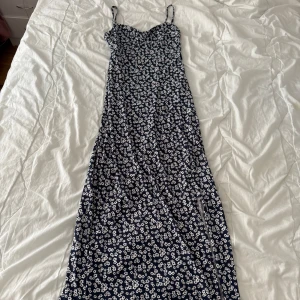 Gina Tricot blommig långklänning - Supersöt långklänning från Gina Tricot. Marinblå botten med vitt blommigt mönster, figurnära passform och snygg slits framtill. Perfekt för dig som gillar en feminin och trendig look. Materialet är mjukt och lätt. Köptes ett tag sen men kom nästan aldrig till användning och säljs inte mer🌸