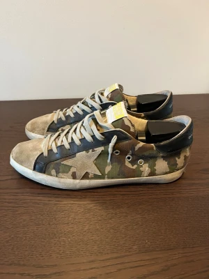 Golden Goose Camo  - Golden Goose Superstars ⭐️                           Skick: 6,5/10. Finns fortfarande liv i dem och sulan är intakt, men sliten.                                              Storlek 45, men passar ockås 45,5.                       Mycket eftertraktad colorway (camouflage)           Perfekta beaters som fortfarande är svinsnygga.