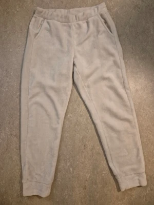 Mjukisbyxor - Supermysiga beige mjukisbyxor från Kappahl i storlek M. Byxorna har en loose passform, resår i midjan och muddar vid bensluten. Tillverkade i mjukt fleece-material, perfekta för chill hemma. Två sidofickor för mobilen eller nycklar. Har en liten svart fläck.