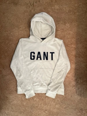 Vit Gant hoodie - Säljer en vit Gant hoodie i storlek 158/164 cm (13-14 år) och befinner sig i mycket bra skick. Dock små defekter på fickan på framsidan och i luvan (se bild 4 & 5), men väldigt svårt att märka av
