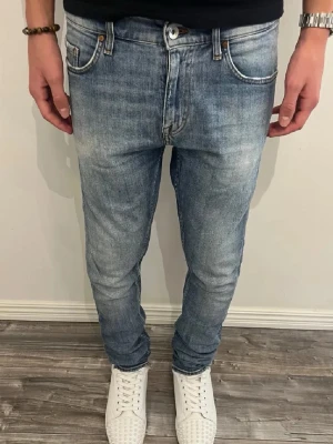 Tiger of Sweden Pistolero jeans blå - Snygga Tiger of Sweden Pistolero jeans i ljusblå tvätt med klassisk femficksdesign och orangea sömmar. Modellen har en slim passform och raka ben, tillverkade i mjuk bomull. Perfekta för dig som gillar stilrena och moderna jeans.