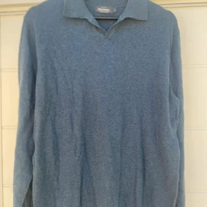 Blå pikétröja Dressmann Supima L - Blå långärmad pikétröja från Dressmann i storlek L, tillverkad av mjuk Supima bomull. Tröjan har klassisk krage och ribbad kant vid halsen. Perfekt för dig som gillar stilrena och bekväma plagg med enkel design.