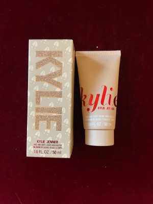 Kylie Jenner Face & Body Liquid Highlighter - Flytande highlighter för ansikte och kropp från Kylie Jenner. Kommer i en beige tub med röd text och en matchande kartong med glitterdetaljer. Innehåller 50 ml. Perfekt för att ge glow och lyster till huden. Snygg design som känns lyxig och trendig.
