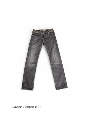Jacob Cohen 622 grå jeans - Snygga grå jeans från Jacob Cohen, modell 622. Klassisk femficksdesign med silverfärgade knappar och broderad modellbeteckning. Jeansen har rak passform och är tillverkade i mjukt denimtyg med diskret tvättad look. Perfekta för dig som gillar stilrena och tidlösa jeans.